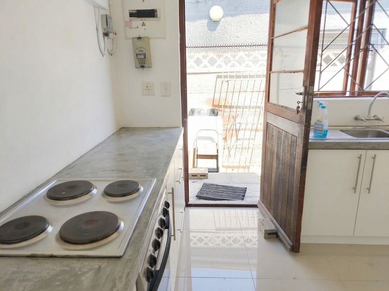 A functional kitchen featuring concrete countertops, a built-in electric hob and oven, white cabinetry, and direct access to an outdoor area.