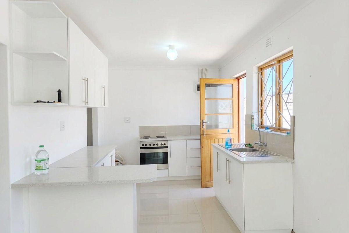 A clean and functional kitchen featuring white cabinetry, stone countertops, a stainless steel sink, and a freestanding stove with direct access to the exterior.
