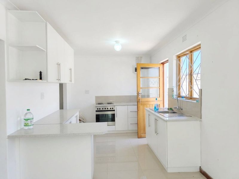 A clean and functional kitchen featuring white cabinetry, stone countertops, a stainless steel sink, and a freestanding stove with direct access to the exterior.