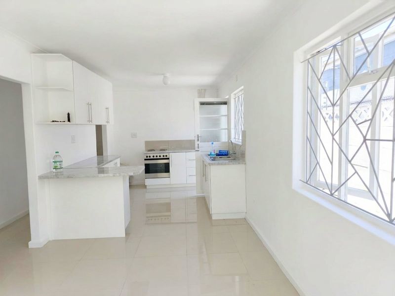 A bright, empty kitchen featuring white cabinetry, stone-look countertops, a freestanding oven, and tiled flooring with security bars on the windows.