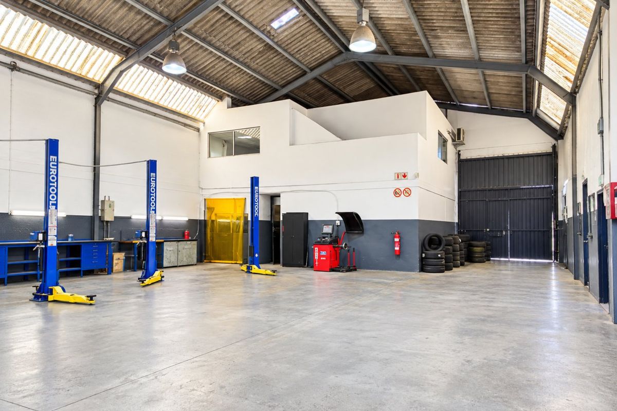 Spacious industrial workshop featuring high ceilings with skylights, concrete flooring, two-post vehicle lifts, and a mezzanine level, suitable for automotive or light industrial operations.
