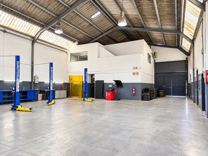 Spacious industrial workshop featuring high ceilings with skylights, concrete flooring, two-post vehicle lifts, and a mezzanine level, suitable for automotive or light industrial operations.