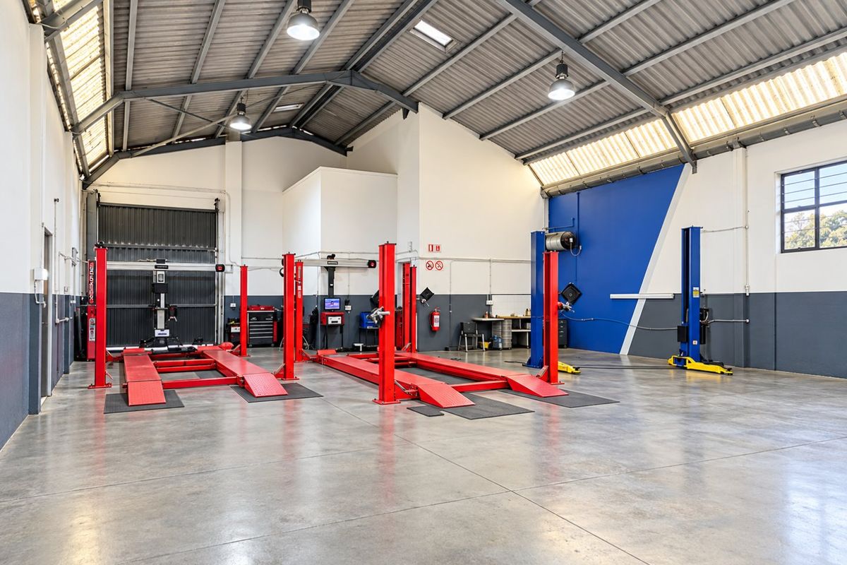 Spacious industrial workshop featuring high ceilings with exposed steel trusses, concrete flooring, multiple vehicle lifts, and integrated skylights for natural illumination.
