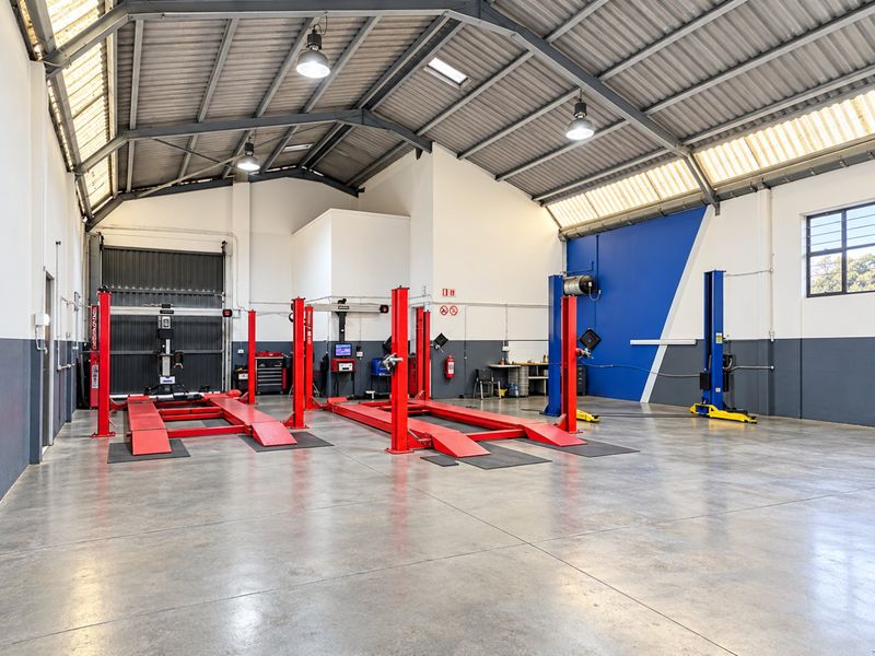 Spacious industrial workshop featuring high ceilings with exposed steel trusses, concrete flooring, multiple vehicle lifts, and integrated skylights for natural illumination.