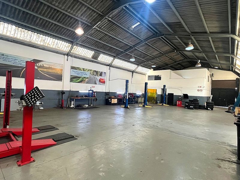 Spacious industrial workshop featuring high ceilings with exposed steel trusses, concrete flooring, and multiple built-in vehicle lifts for automotive maintenance operations.