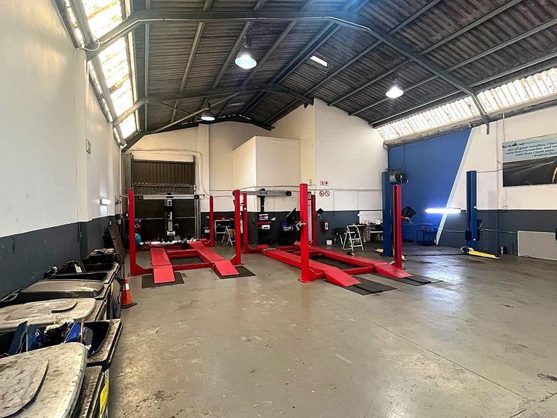 Spacious industrial garage workshop featuring multiple vehicle lifts, high ceilings with exposed trusses, skylights, and durable concrete flooring.