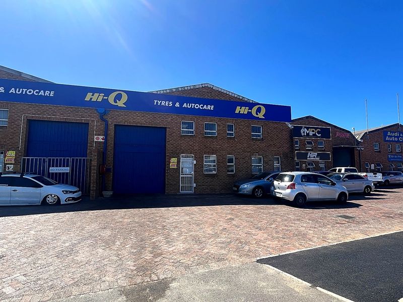Front elevation of an industrial complex featuring brick facade, multiple roller shutter doors, and a paved forecourt area with signage.