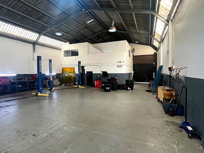 Spacious industrial workshop featuring two-post vehicle lifts, high ceilings with skylights, concrete flooring, and a mezzanine office level.