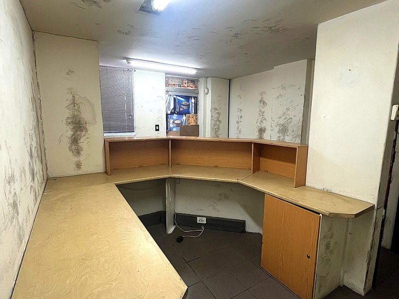 An empty office space featuring a built-in reception desk, tiled flooring, and fluorescent lighting, currently requiring significant wall repairs and cosmetic refurbishment.