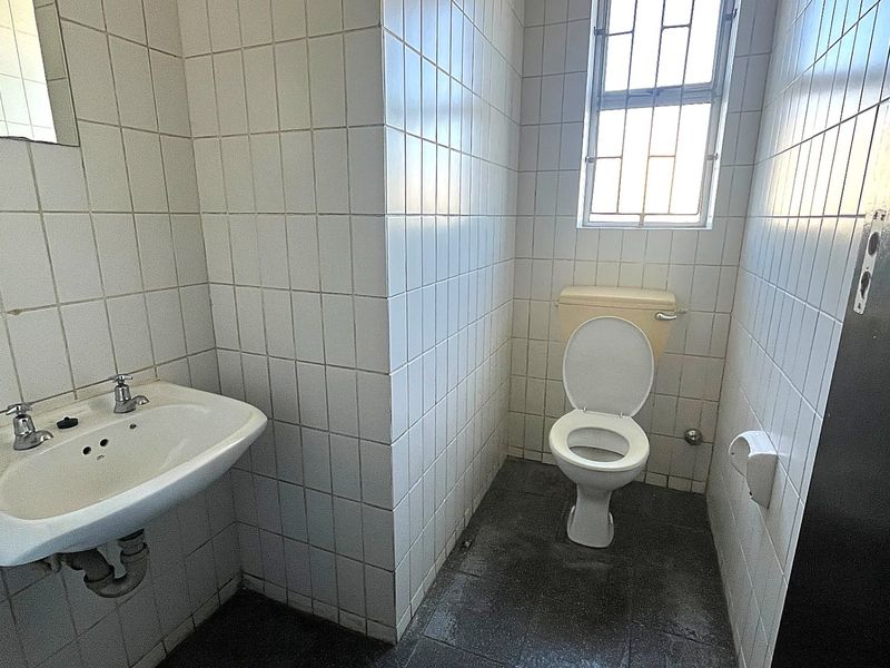 A functional bathroom featuring white wall tiles, a pedestal basin, and a toilet, requiring cosmetic updates to improve its overall condition.