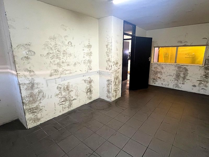 An empty utility space featuring tiled flooring and fluorescent lighting, currently requiring significant wall surface repairs and repainting.