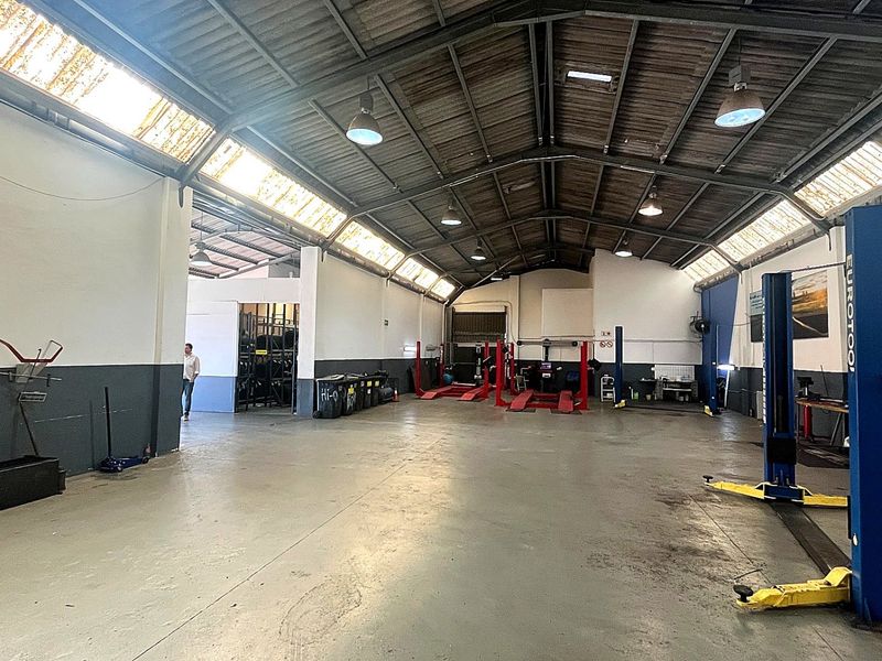 Spacious industrial workshop featuring high ceilings with exposed steel trusses, integrated skylights, and multiple vehicle service lifts installed on concrete flooring.