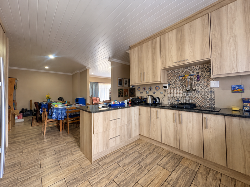 Open-plan kitchen featuring wood-look cabinetry, granite countertops, and a decorative tile backsplash, seamlessly flowing into the adjacent dining area.