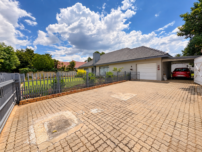 Front exterior view of the house featuring a paved driveway, metal fencing, a single garage, and an attached carport.