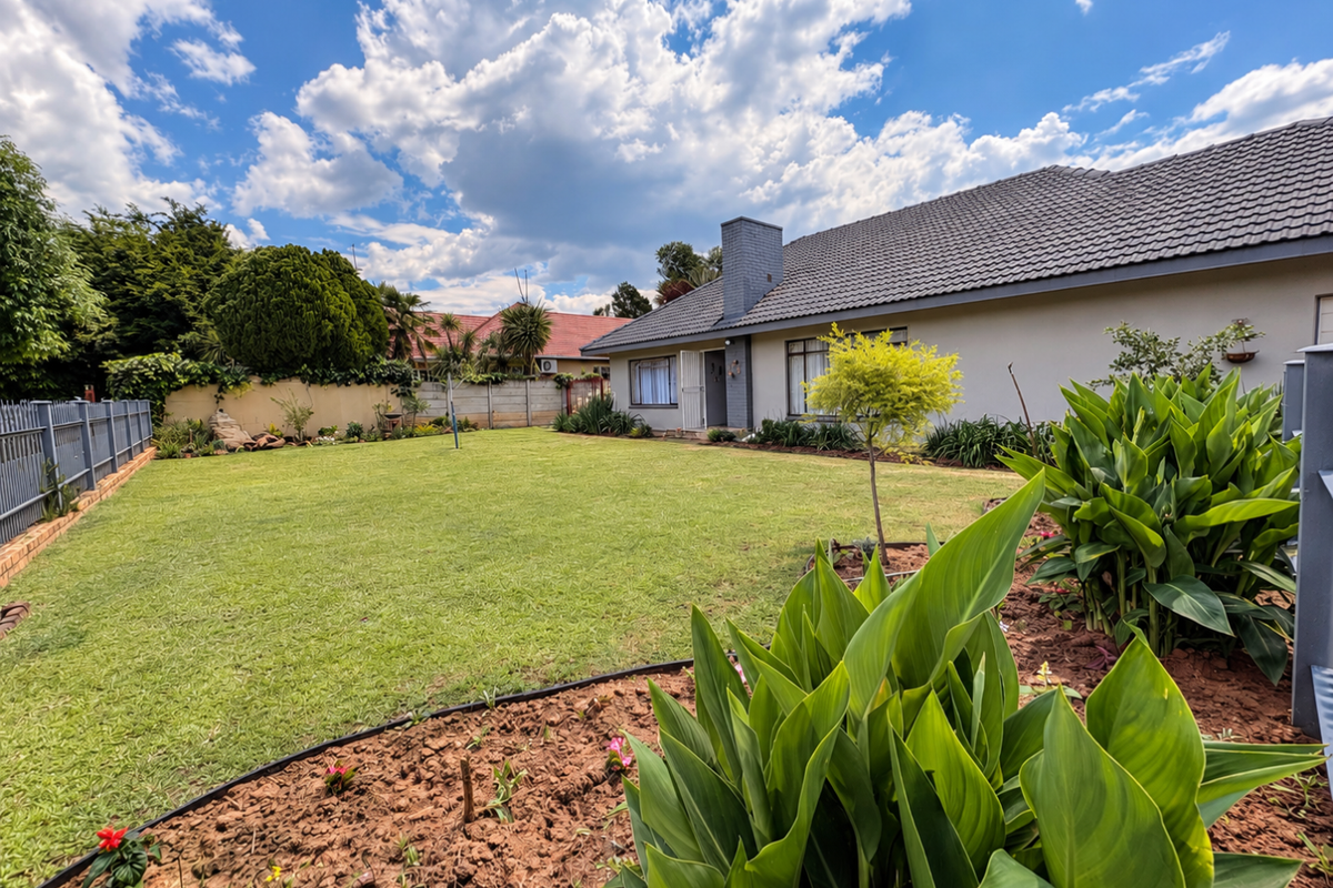 A well-maintained rear garden featuring a spacious lawn, landscaped flower beds, and a clear view of the house exterior with a tiled roof.