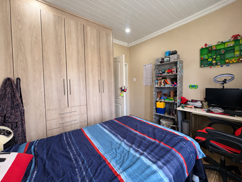 A functional bedroom featuring extensive light wood-grain built-in wardrobes and a classic tongue and groove ceiling finish.