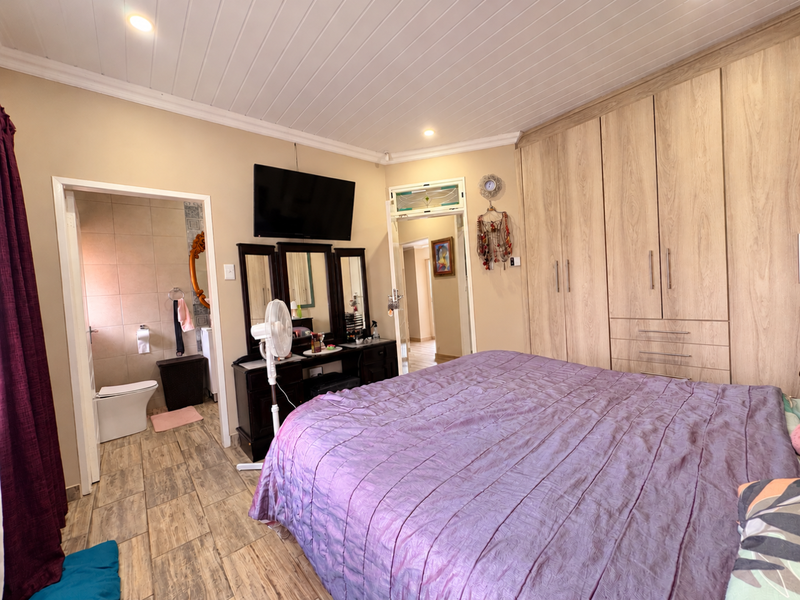Spacious bedroom featuring built-in wooden cupboards, tiled flooring, a tongue and groove ceiling, and direct access to an en-suite bathroom.