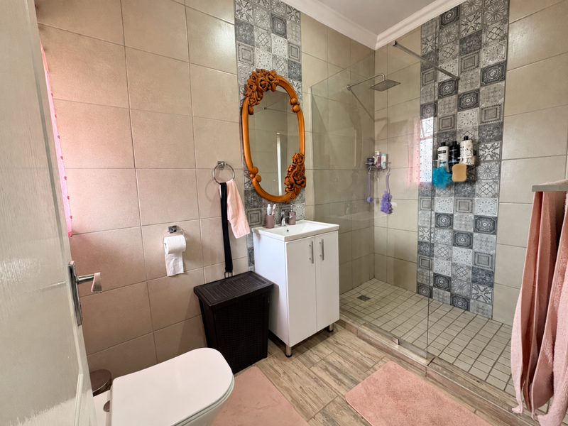 Modern bathroom featuring a walk-in shower with rainfall shower head, decorative feature tiling, vanity basin, and toilet with neutral floor tiles.