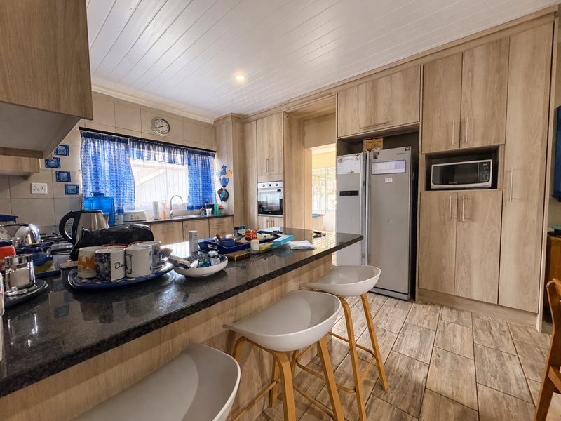 A well-appointed kitchen featuring light wood cabinetry, granite countertops, a central island, and built-in appliances, complemented by tiled flooring and a clean ceiling finish.