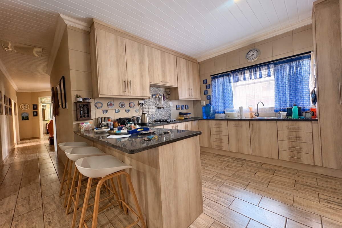 A functional kitchen featuring light wood-look cabinetry, granite countertops, a central island, and tiled flooring with a classic tongue and groove ceiling finish.