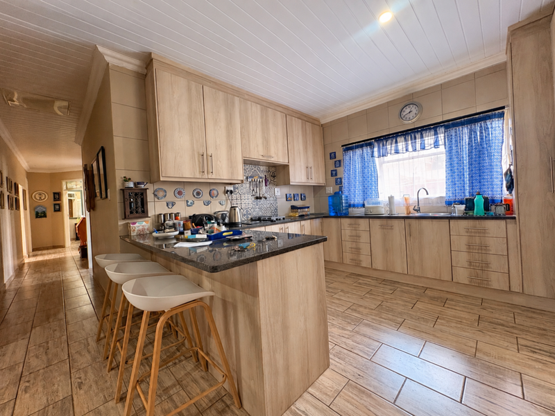 A functional kitchen featuring light wood-look cabinetry, granite countertops, a central island, and tiled flooring with a classic tongue and groove ceiling finish.
