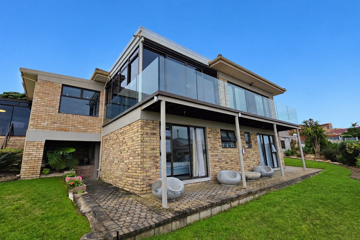 Rear view of a two-story brick house featuring an upper-level balcony with a glass balustrade, sliding doors, and a paved patio area.