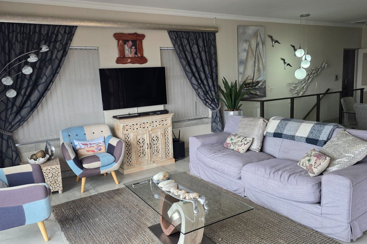 A comfortable living room featuring tiled flooring, modern pendant lighting, and an open-plan layout with a staircase railing visible in the background.