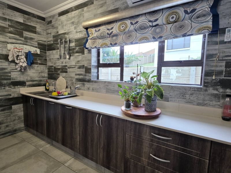 A functional kitchen featuring dark wood-finish cabinetry, stone countertops, a stainless steel sink, and decorative tiled wall finishes.