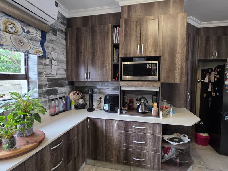 A well-maintained kitchen featuring modern wood-grain cabinetry, stone countertops, built-in microwave, and tiled flooring with an integrated air conditioning unit.