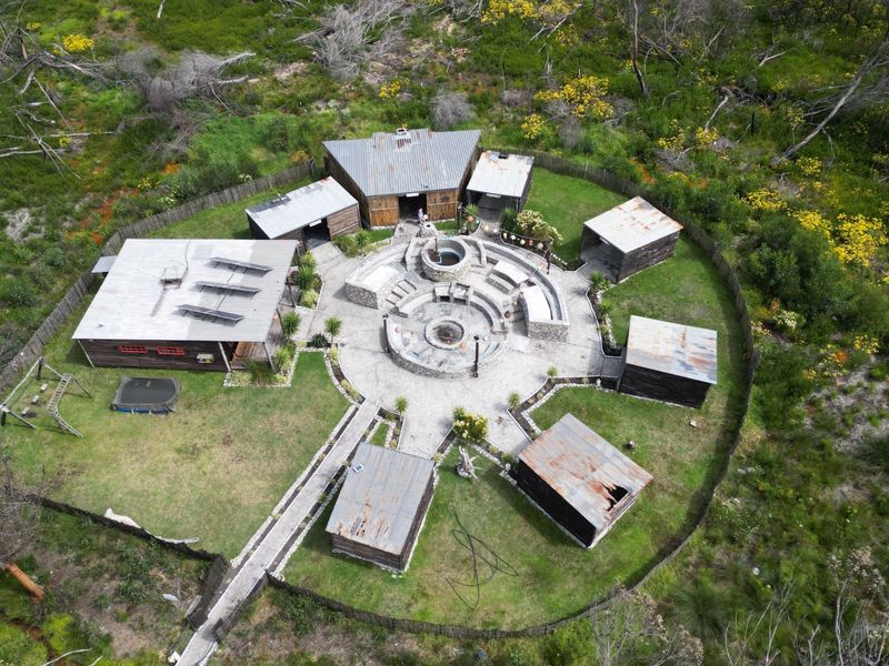 Aerial view of a rural property featuring multiple detached structures arranged around a central stone fire pit and outdoor entertainment area.