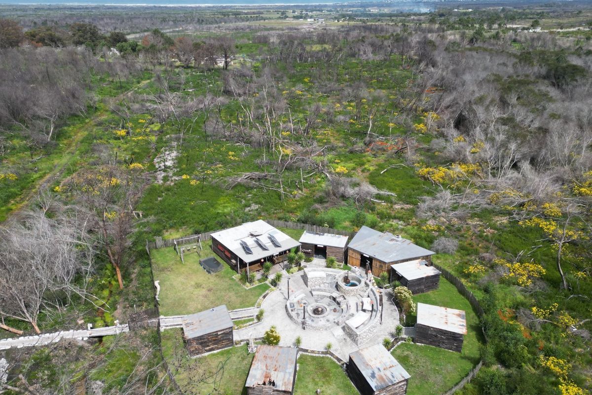 Aerial view of a rural farm property featuring multiple outbuildings arranged around a central stone fire pit area with solar panels installed.