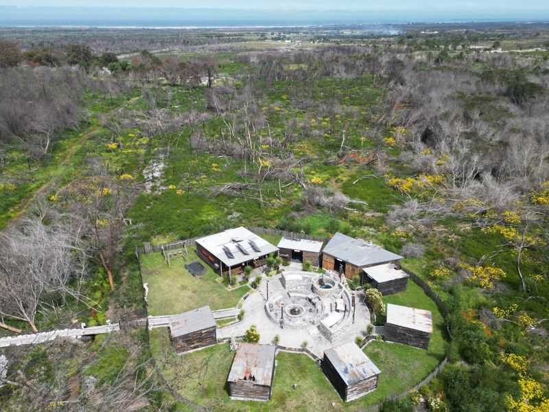 Aerial view of a rural farm property featuring multiple outbuildings arranged around a central stone fire pit area with solar panels installed.