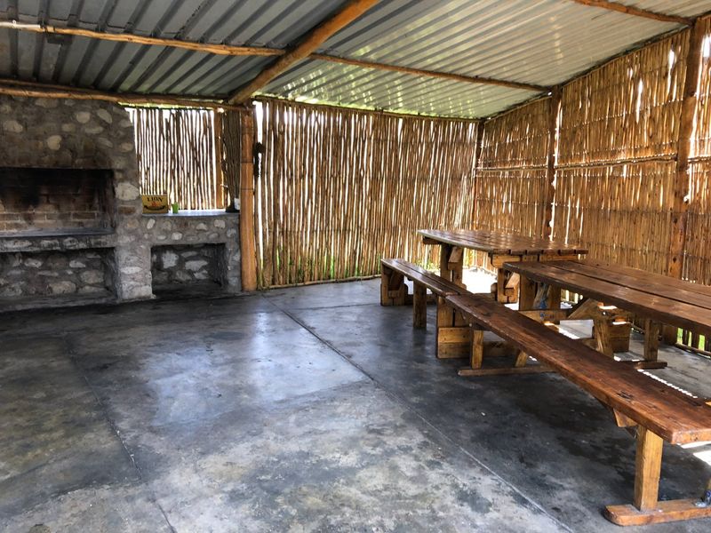 Rustic outdoor entertainment area featuring a built-in stone braai, corrugated roof, and reed walling, providing a functional space for farm-style gatherings.