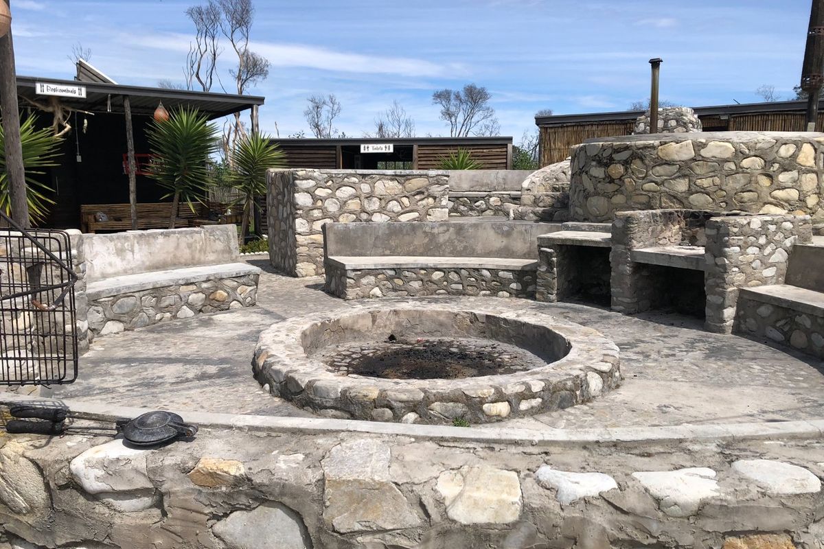 Outdoor entertainment area featuring a central stone fire pit, built-in stone seating, and a dedicated stone braai facility.