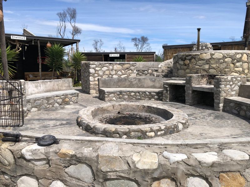 Outdoor entertainment area featuring a central stone fire pit, built-in stone seating, and a dedicated stone braai facility.