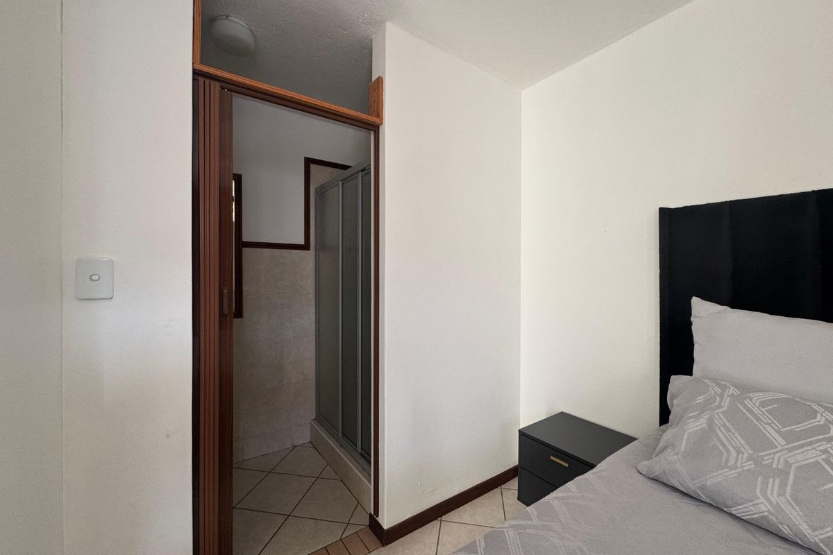 A bedroom featuring an en-suite bathroom with a shower cubicle, tiled flooring, and neutral wall finishes.