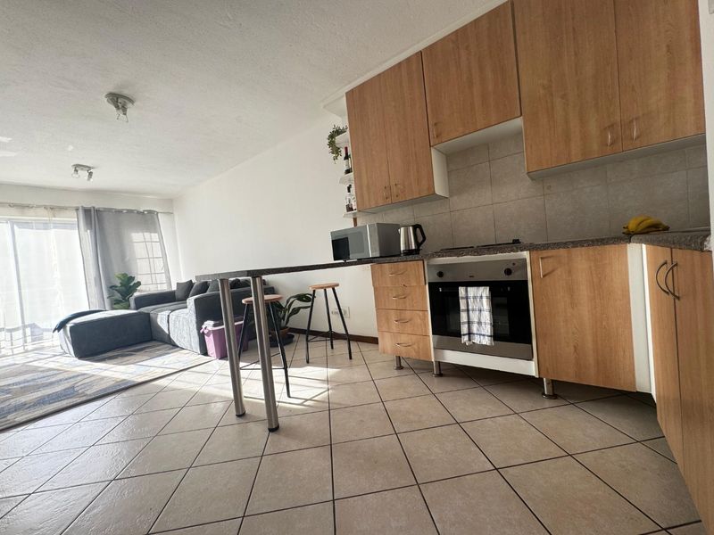 Open-plan living area featuring a kitchen with wood-finish cabinetry, built-in oven, breakfast bar, and tiled flooring, leading to a bright lounge with sliding door access.