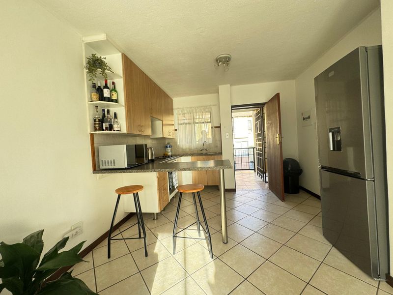 Compact kitchen featuring light wood cabinetry, a breakfast bar, ceramic tiled flooring, and direct access to an outdoor balcony area.