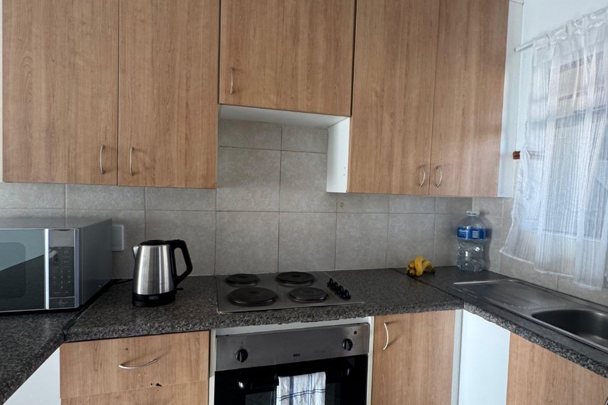 A functional kitchen featuring wood-look laminate cabinetry, granite countertops, a built-in oven with electric hob, and tiled flooring.
