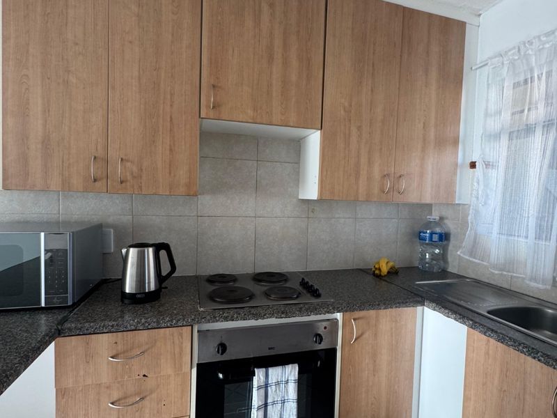 A functional kitchen featuring wood-look laminate cabinetry, granite countertops, a built-in oven with electric hob, and tiled flooring.