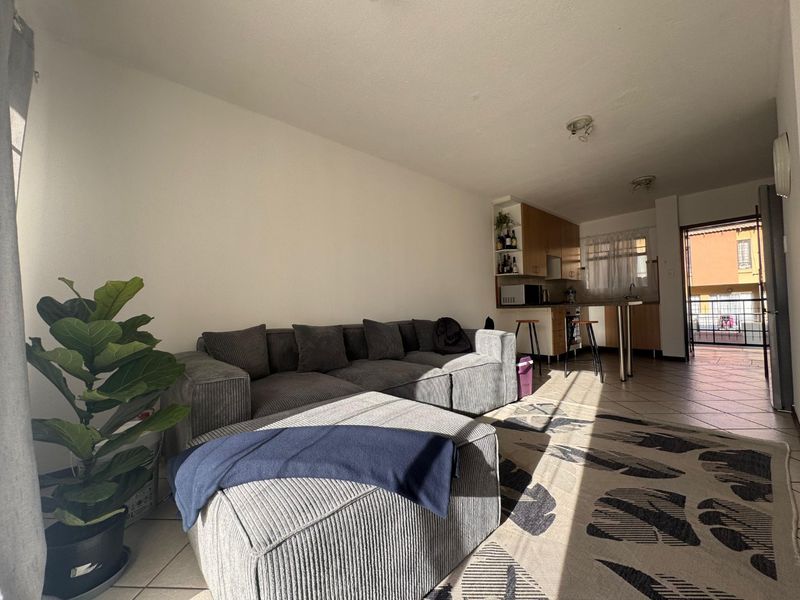 Open-plan living area featuring tiled flooring and a functional kitchen with built-in cabinetry and a breakfast counter, leading to an outdoor balcony.