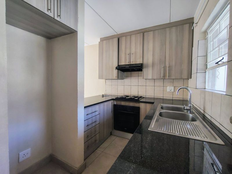 A clean and functional kitchen featuring modern wood-finish cabinetry, granite countertops, a built-in oven, hob, and a double bowl sink.