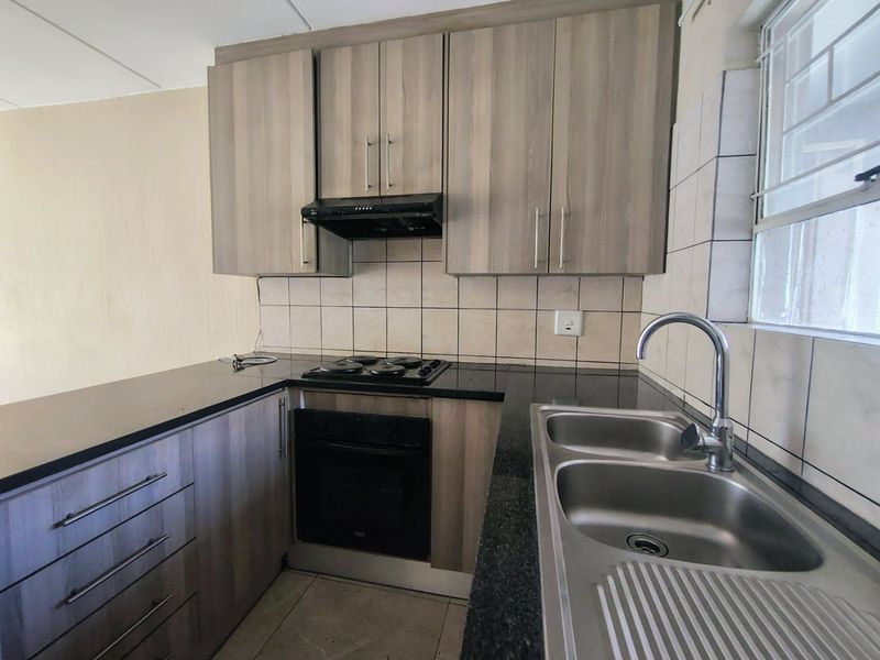 A functional kitchen featuring wood-look cabinetry, black countertops, a built-in oven with hob, and a stainless steel double sink.