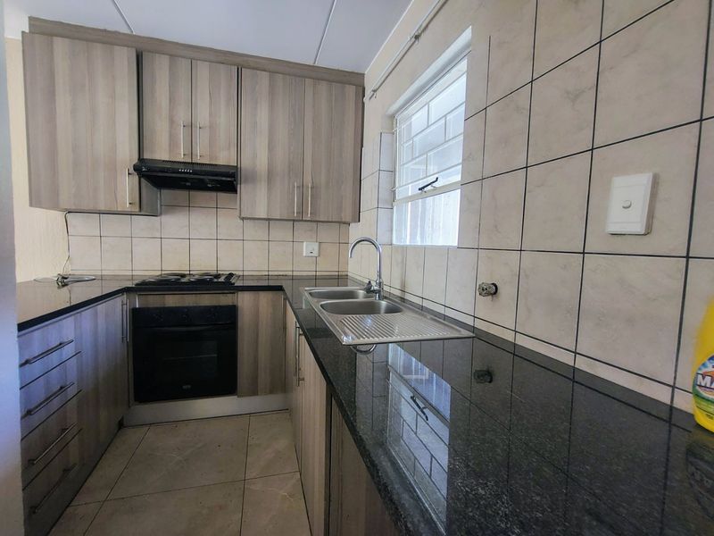 A functional kitchen featuring wood-look cabinetry, granite countertops, a built-in oven and hob, and a tiled backsplash with a double sink.