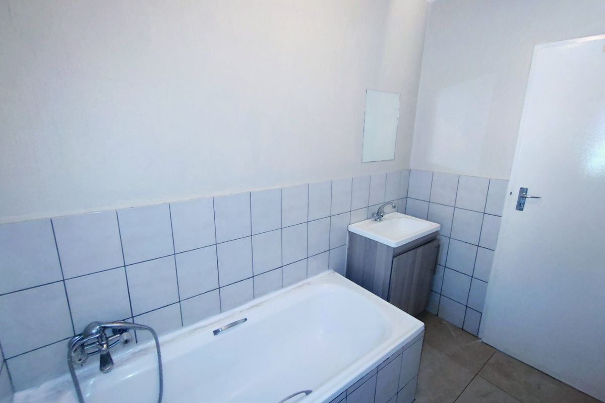 A functional bathroom featuring a bathtub, a vanity cabinet with a washbasin, and neutral wall and floor tiling.