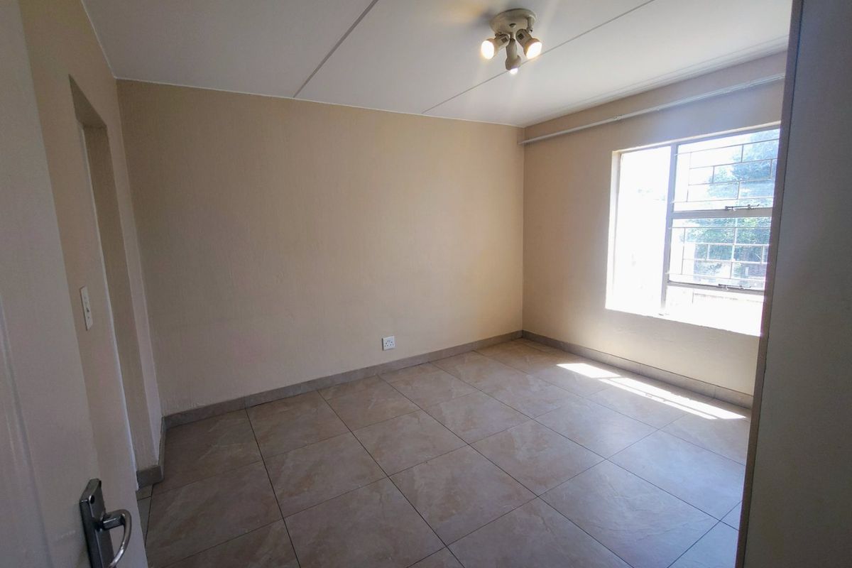 An empty bedroom featuring neutral wall paint, tiled flooring, and a window fitted with security bars.