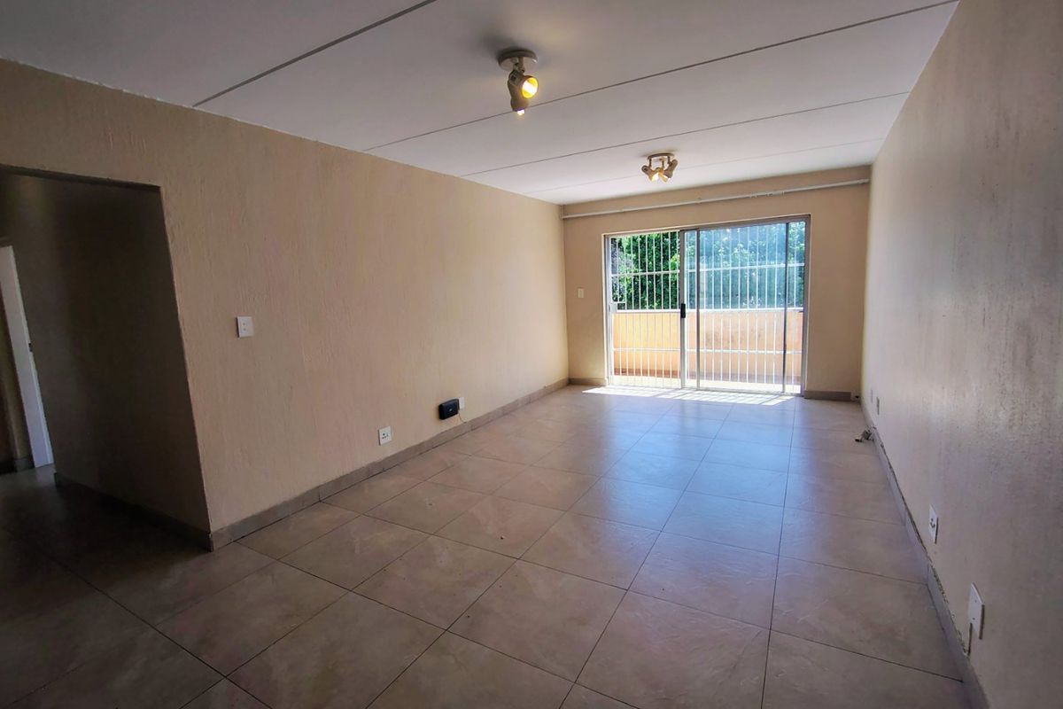 An empty, open-plan living area featuring tiled flooring, neutral walls, and a sliding glass door with security gate leading to an outdoor space.