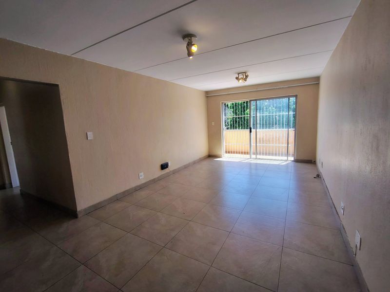 An empty, open-plan living area featuring tiled flooring, neutral walls, and a sliding glass door with security gate leading to an outdoor space.