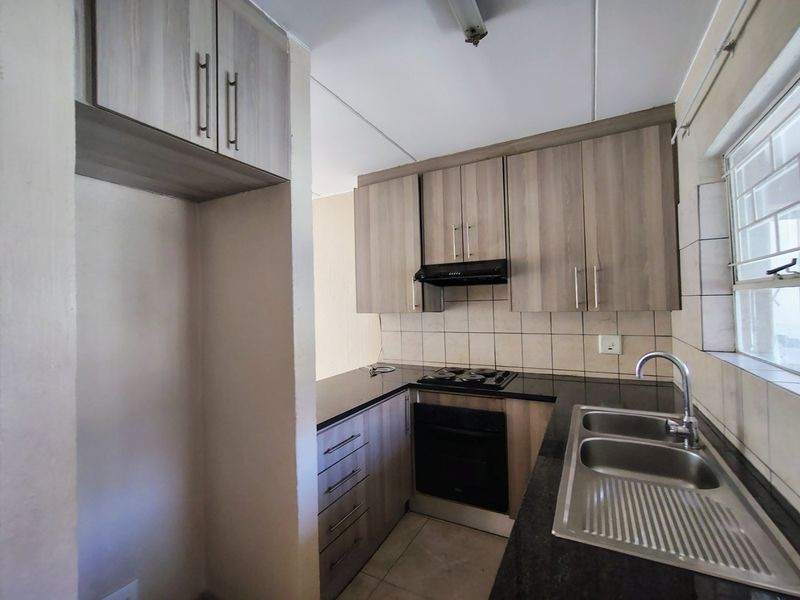A functional kitchen featuring wood-look cabinetry, dark countertops, a built-in oven with hob, and a double bowl sink with tiled backsplash.