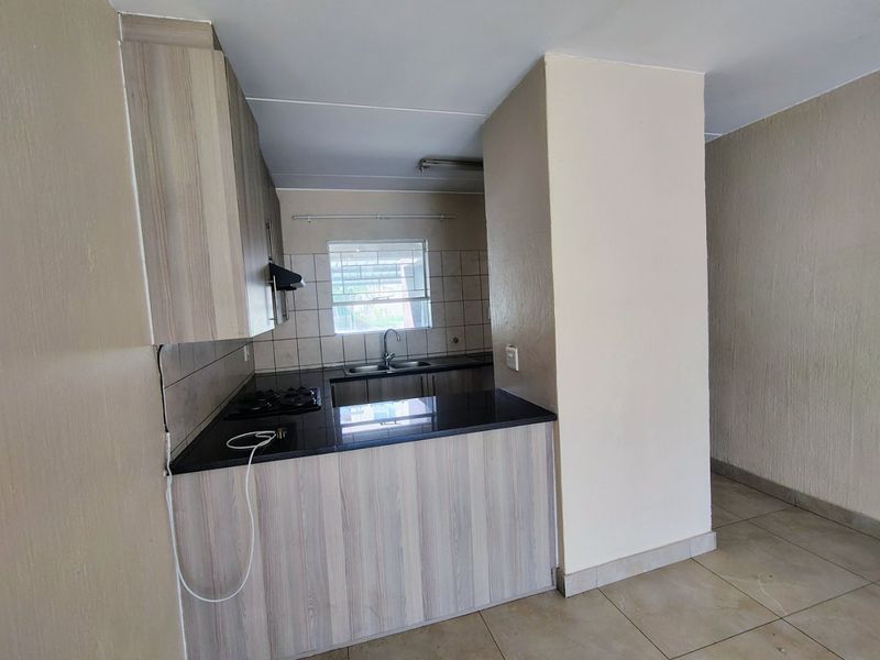 A functional kitchen featuring light wood-finish cabinetry, dark granite countertops, a gas hob with extractor, and tiled flooring in an open-plan layout.